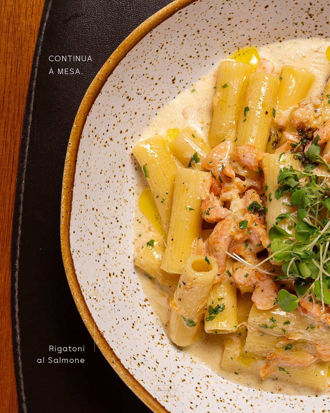 Rigatoni al Salmone em prato de cerâmica pontilhada, com a legenda “Continua à mesa”