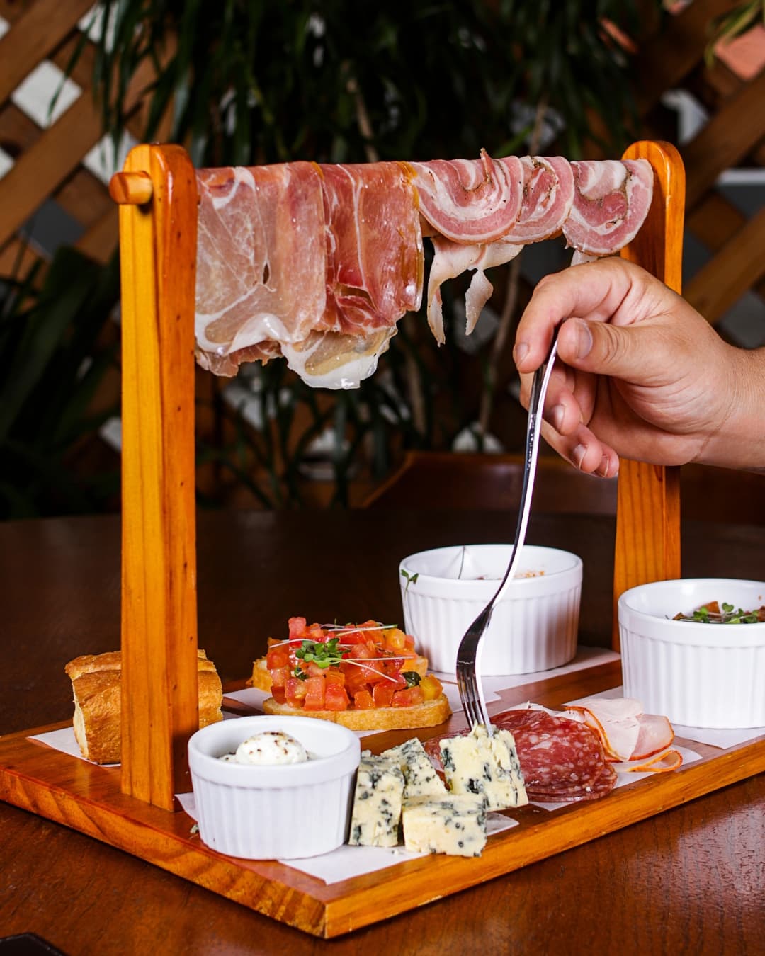 Tábua de frios com presunto parma e pancetta pendurados num varal de madeira, bruschetta, queijo gorgonzola e salame
